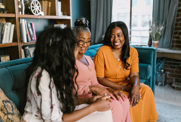 Three women sitting together on a sofa, talking and laughing