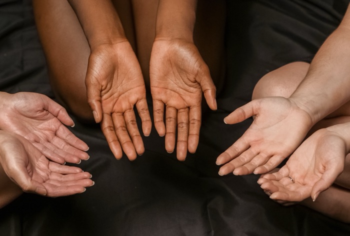 Open palms of several women resting together on dark cloth