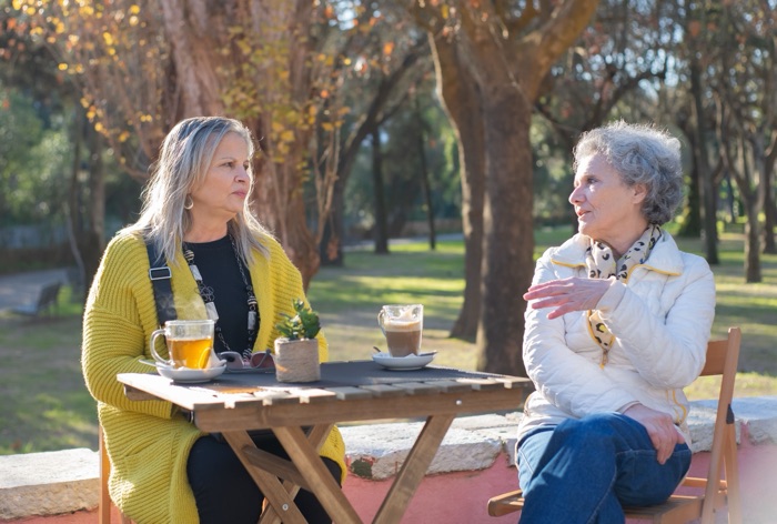 Two women talking over tea at a table in a sunlit park